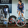 Cyclocross racer on bike warming up on Omnium stationary trainer under team tent in front of vehicle. 