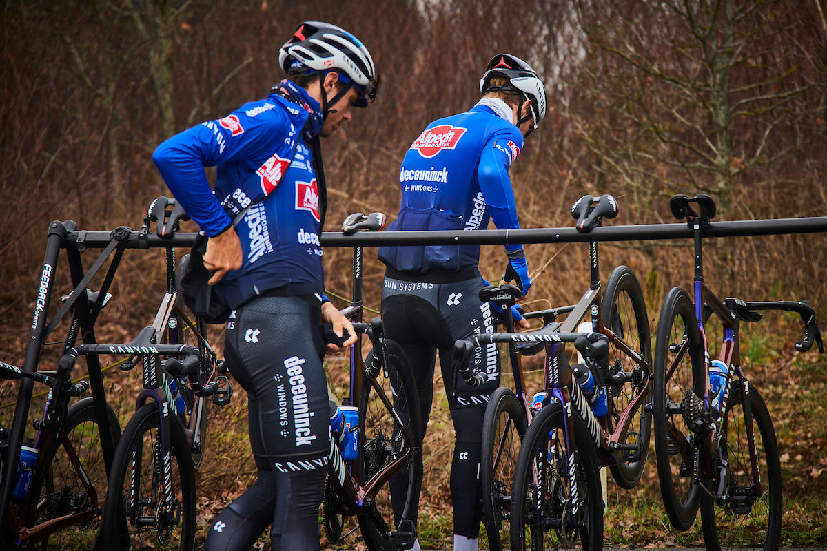 two alpecin deceunick pro cyclists getting their bikes off of a feedback sports a-frame event stand