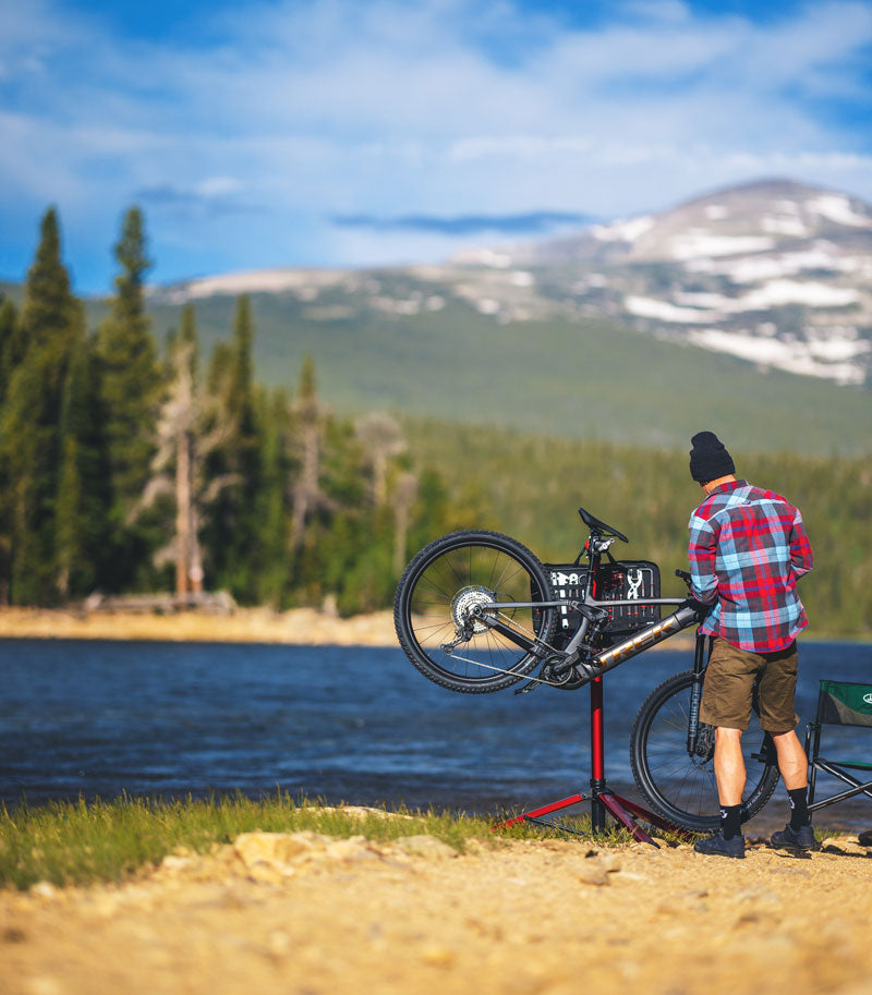 Man working on mountain bike in a bike repair stand outdoors by a lake.