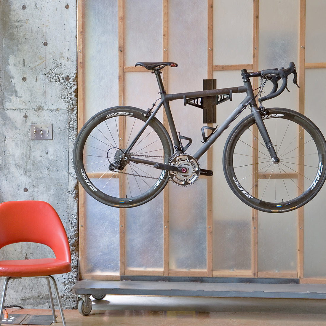 Black road bike suspended on bike storage cradle arms installed on 2x4 wall.