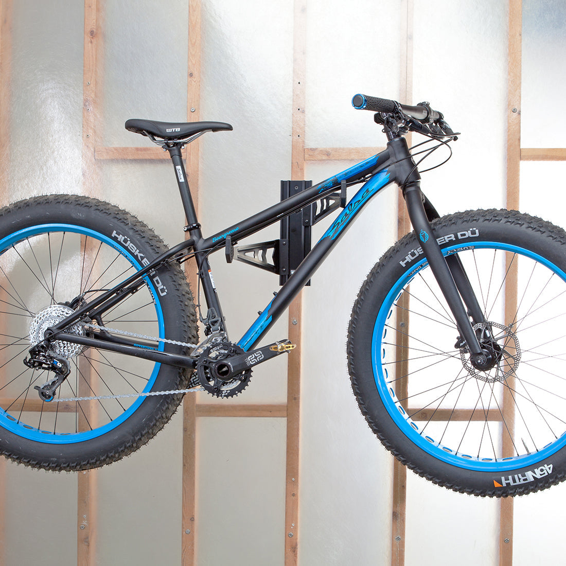 Fat tire mountain bike suspended from wall mount bike storage cradle arms on 2x4 interior wall.