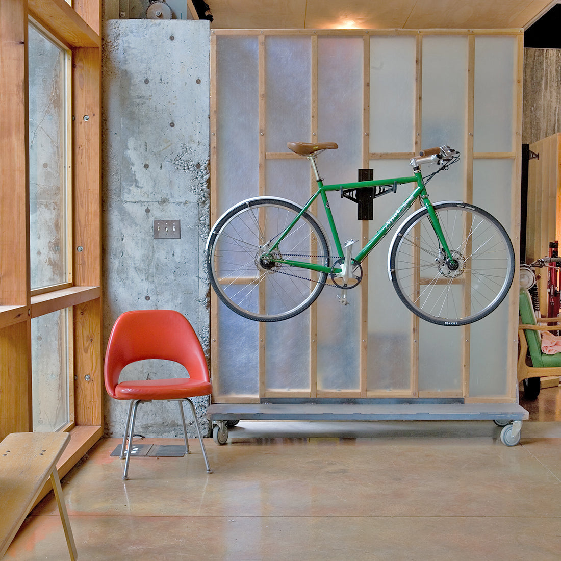 Green town bike suspended on bike cradle arms attached to 2x4 interior stud wall.