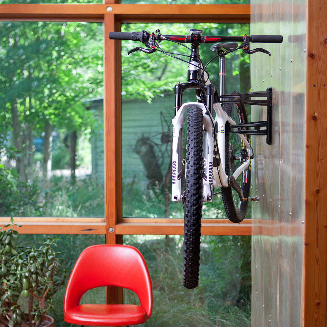 Mountain bike installed on interior wall storage cradle arms with windows in background.