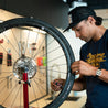 Person in shop using tire valve core tool to install a bike tire valve core with wheel in truing stand.