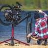Person working on mountain bike in bike repair stand outdoors next to lake.