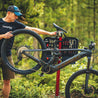 Person working on mountain bike outdoors in forest with bike in repair stand.