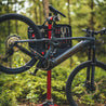 Grey mountain bike clamped in red bike repair stand with tool kit installed for use outdoors.
