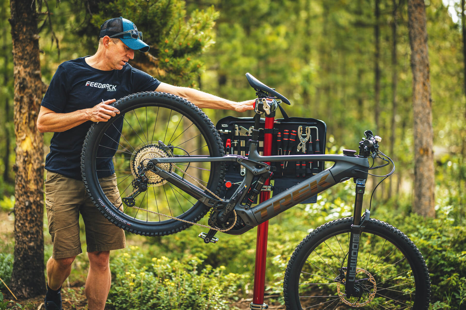 Man working on mountain bike with bike in a repair stand outdoors.