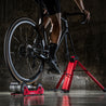 Rider on black road bike mounted on Omnium stationary trainer in dark background studio setting.