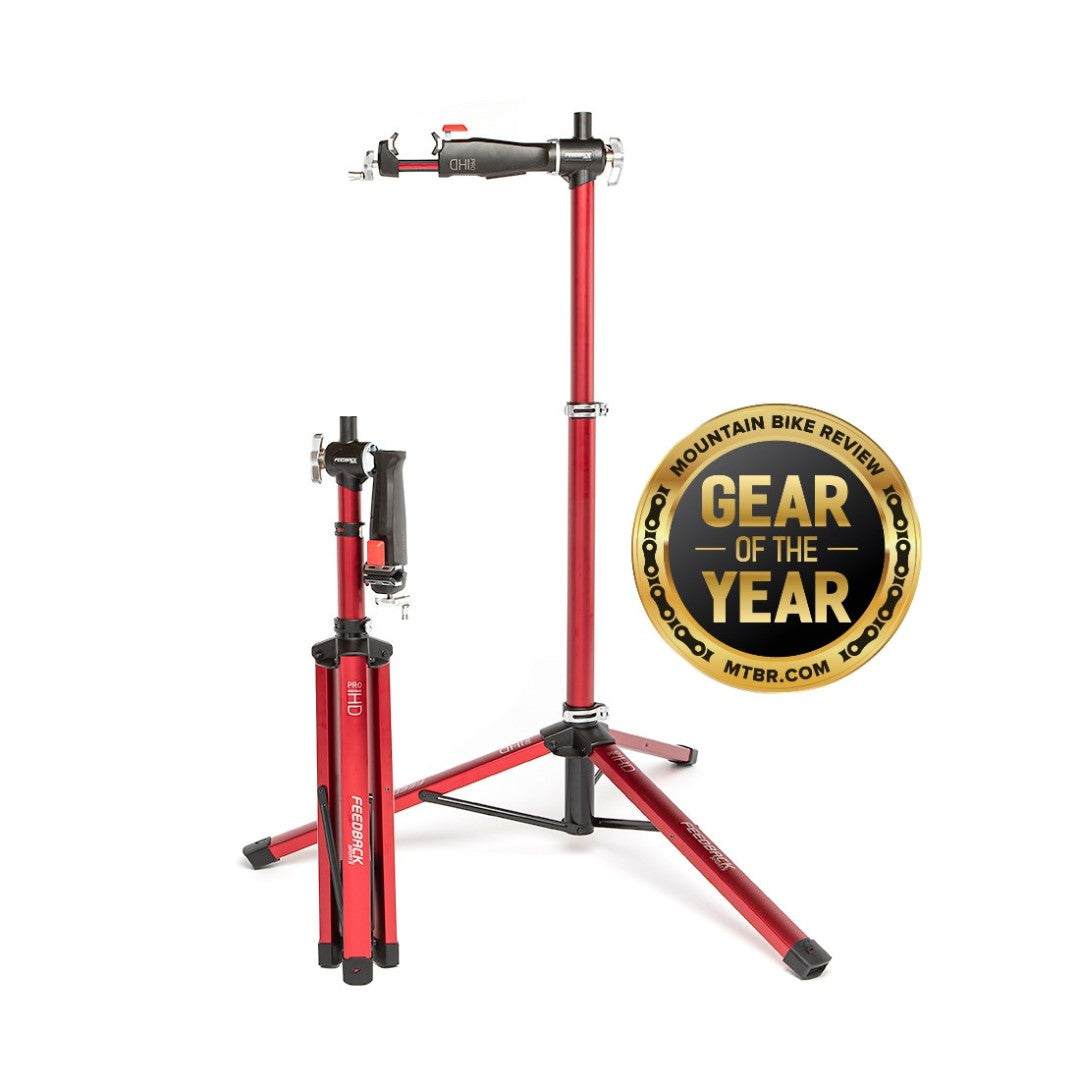 Feedback Pro Mechanic HD Bike Repair Stand both open and folded into compact travel form next to a "Gear of the Year" award from MTBR.com mountain bike review